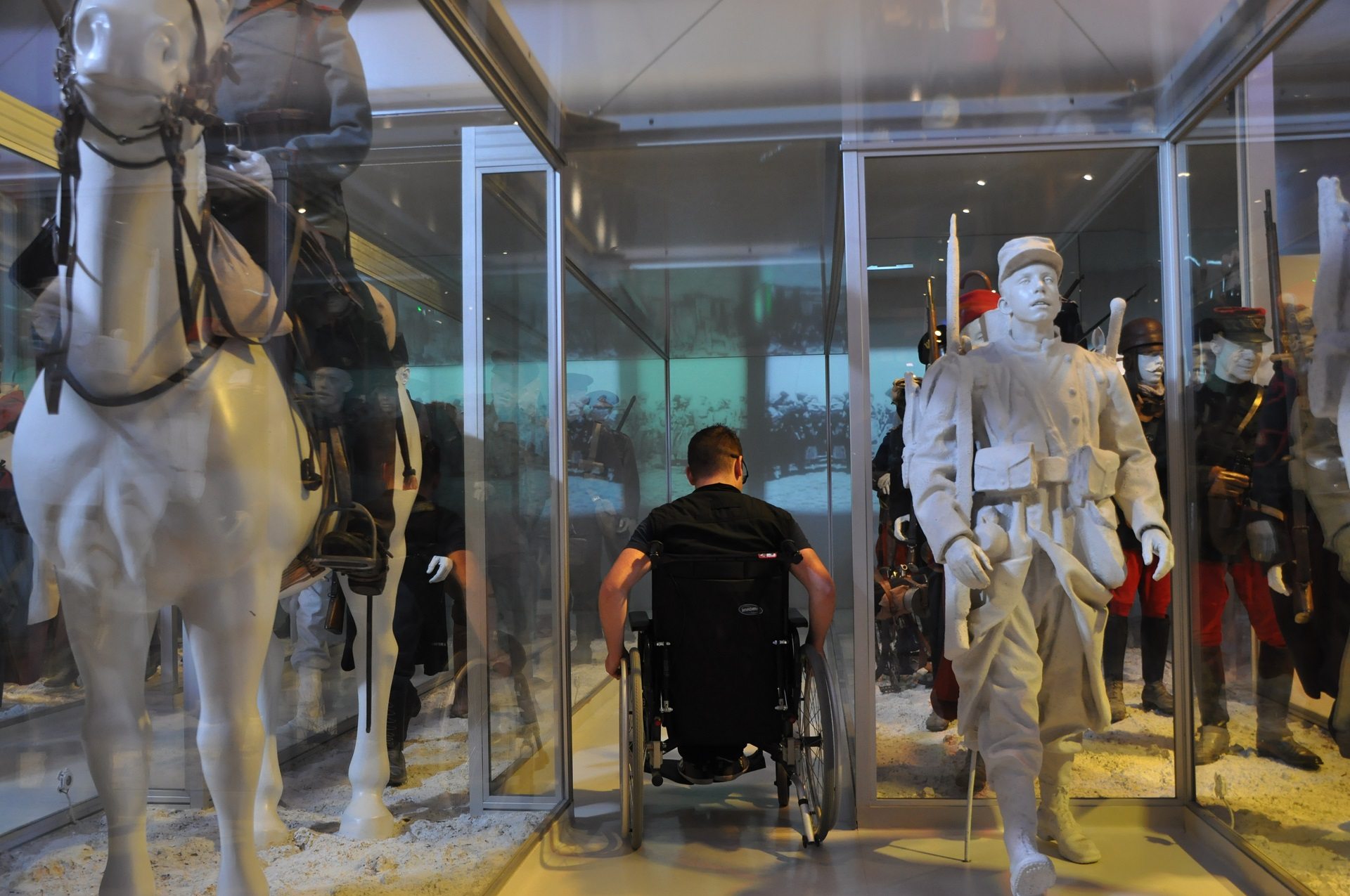 visiteur en fauteuil roulant entre deux rangées de statues de soldats de 1914 au Musée de la Grande Guerre à Meaux